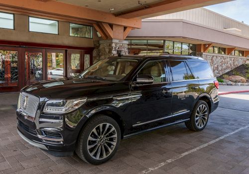A shiny black SUV parked under a covered entrance, near a stone and wood building, with large tinted windows and chrome accents.