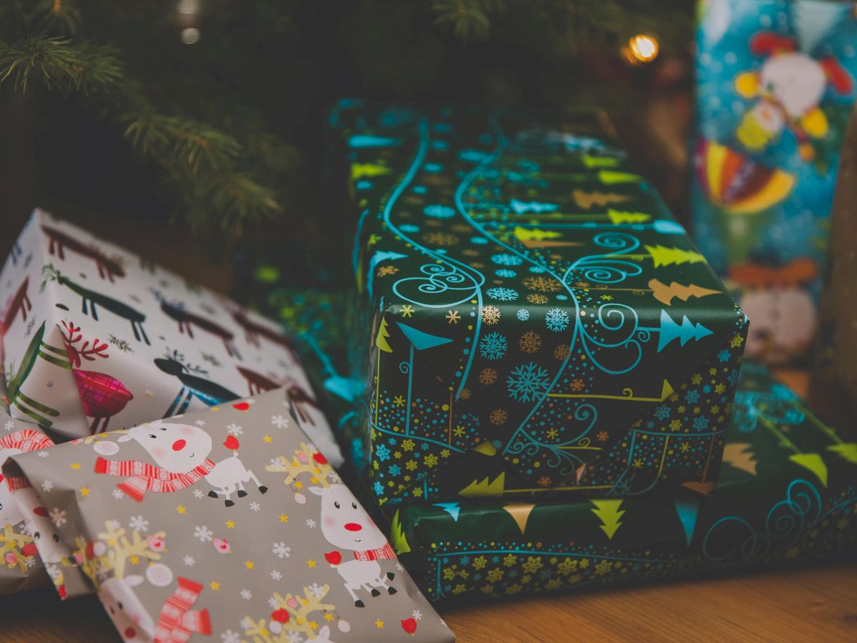 The image shows a group of wrapped Christmas presents in festive holiday paper, placed under a Christmas tree.