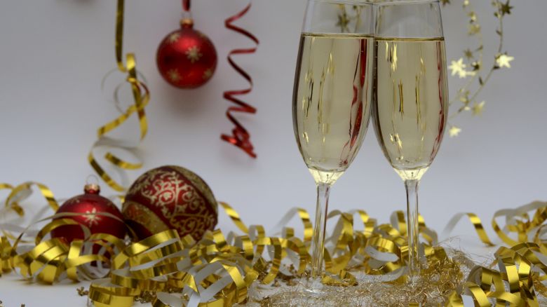 Two champagne flutes, gold streamers and ornaments on a festive backdrop; sparkling celebrations for the New Year or a holiday party.