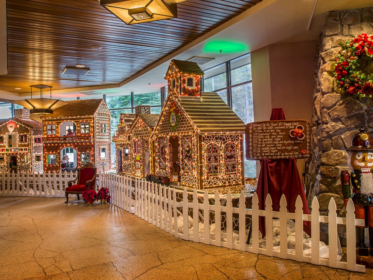 The image features a festive indoor display with gingerbread houses, a white picket fence, a nutcracker figure, and a holiday wreath on a stone wall.