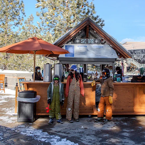 A small ski lodge with a wooden counter, two kids in snowsuits, and adults as staff under a peaked roof, with snow on the ground.