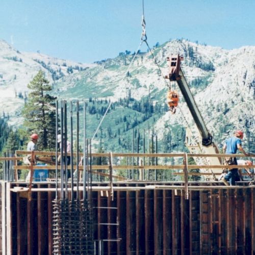 Two workers on a construction site with mountains in the background; a crane and rebar structure are visible in the scene.