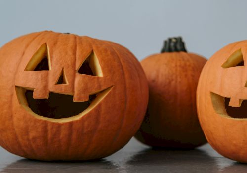 The image shows three pumpkins; two have carved faces, and one is uncarved, all placed on a flat surface.