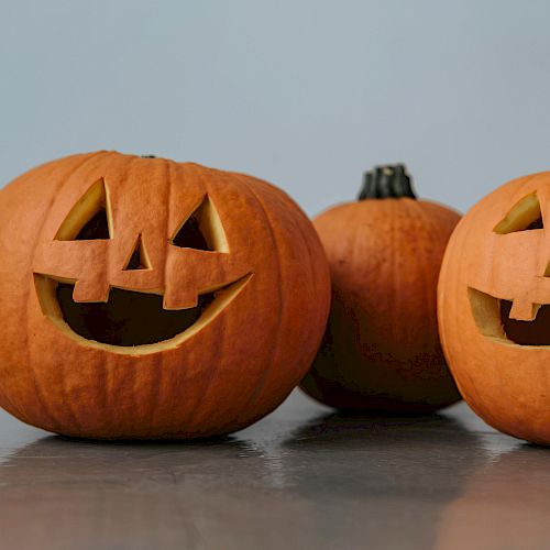 The image shows three pumpkins; two have carved faces, and one is uncarved, all placed on a flat surface.