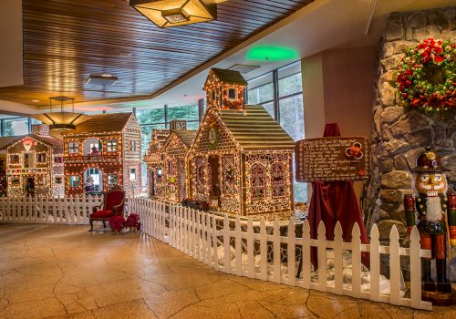 The image shows a festive indoor display featuring gingerbread houses, a white picket fence, a nutcracker statue, and a decorated wreath.