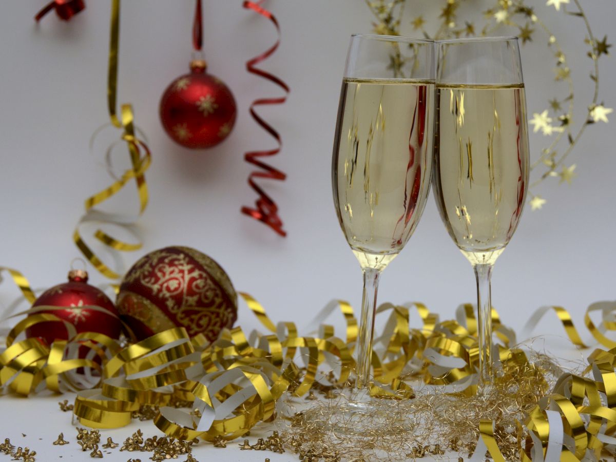 Two champagne glasses surrounded by red ornaments, gold and white ribbons, and star-shaped decorations, creating a festive atmosphere.