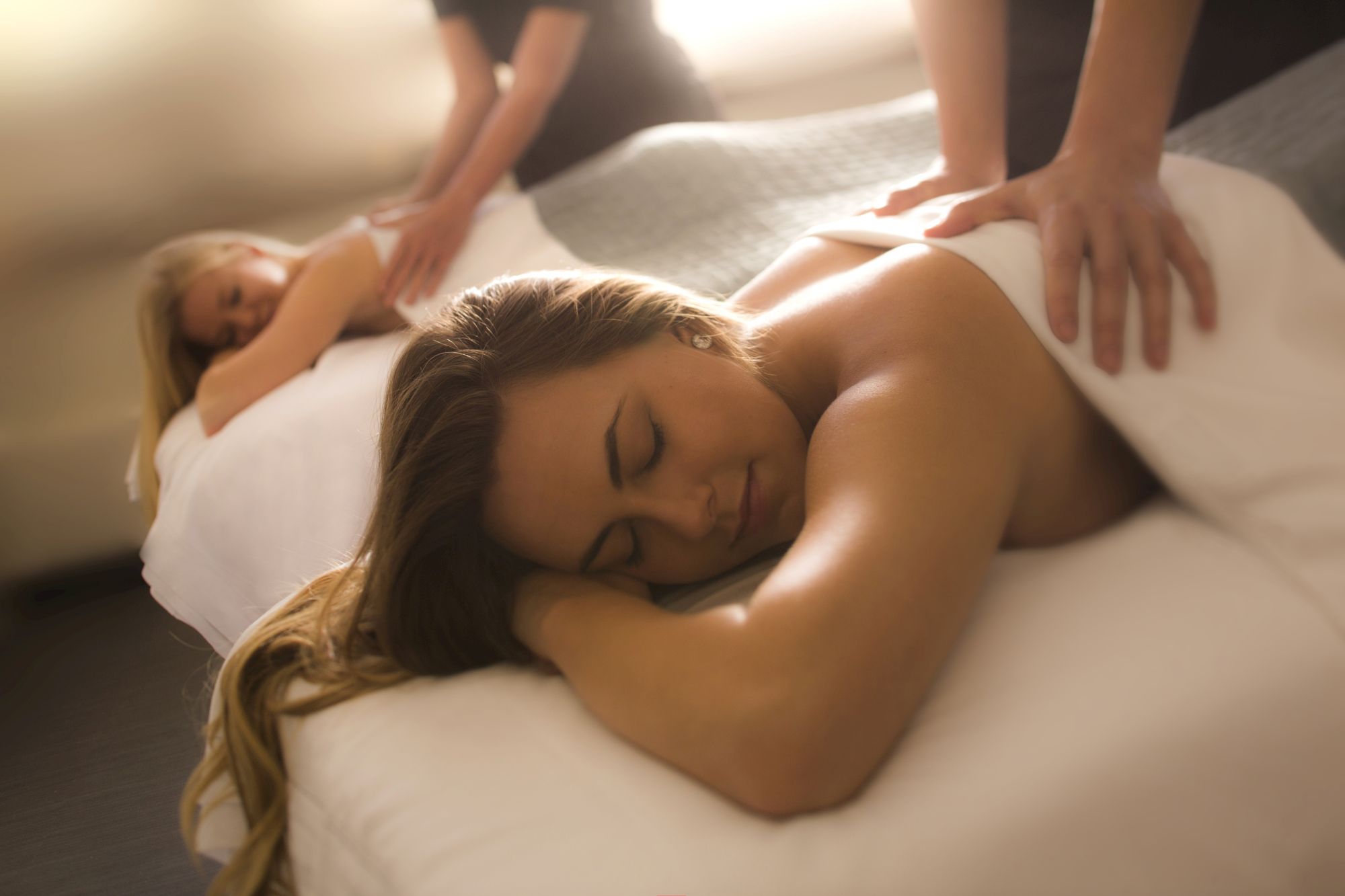 Two people receiving massages on massage tables, both covered with towels, in a serene setting.