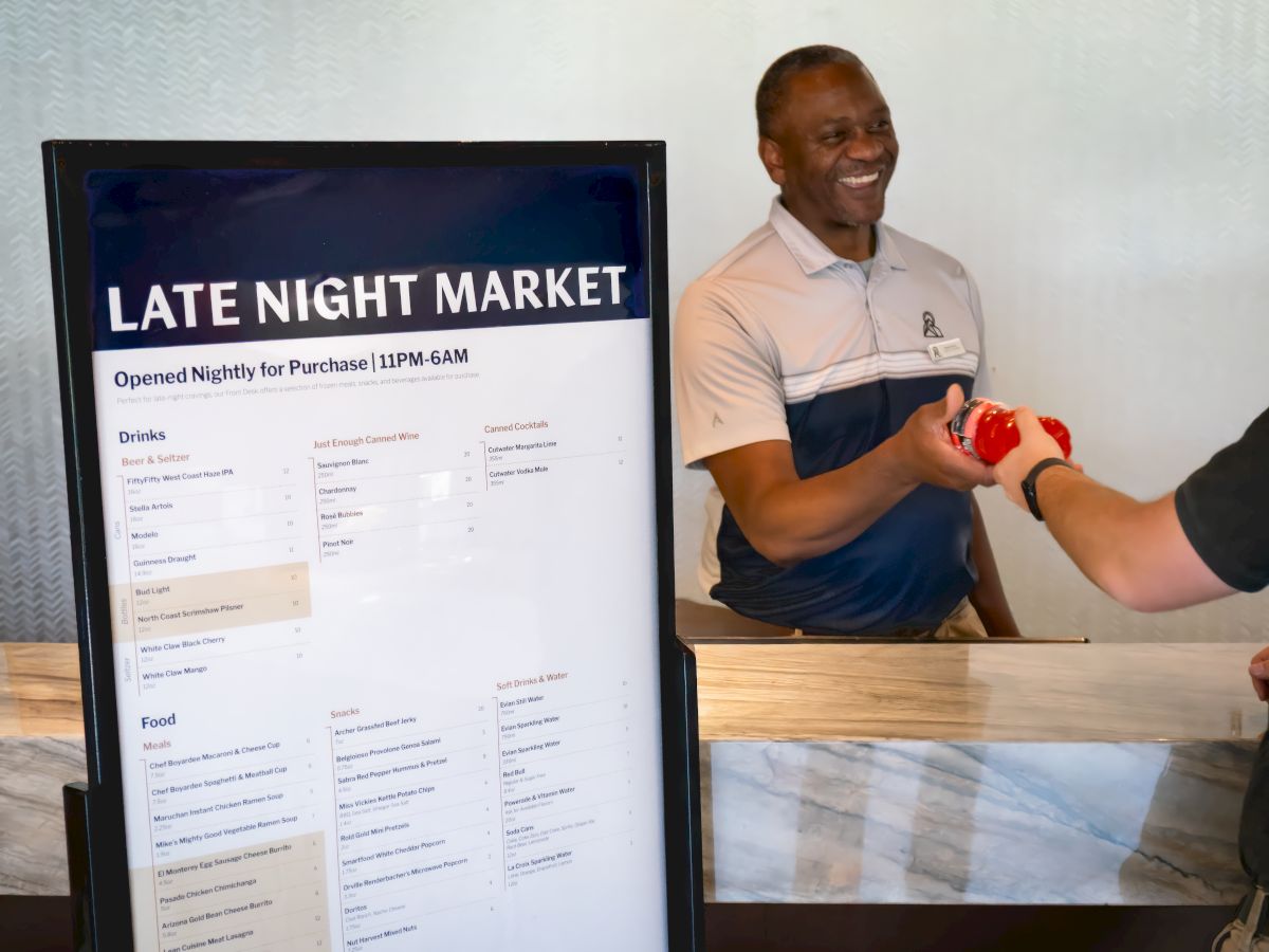A server smiles while pouring a drink beside a &ldquo;Late Night Market&rdquo; menu board.