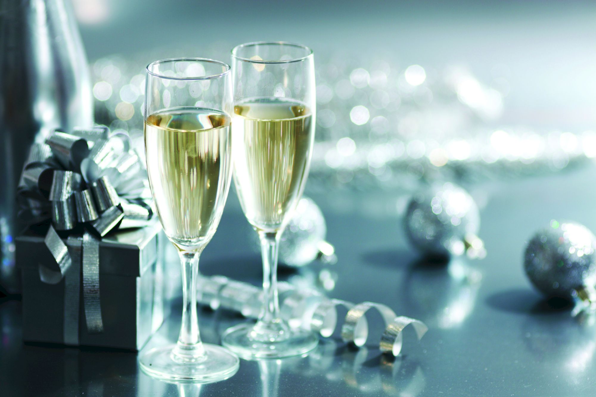 Two champagne glasses, a gift box with a silver ribbon, and decorative silver ornaments create a celebratory scene.