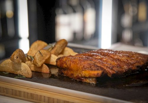 The image shows a roasted meat dish accompanied by wedges of roasted potatoes, garnished and served on a dark platter.