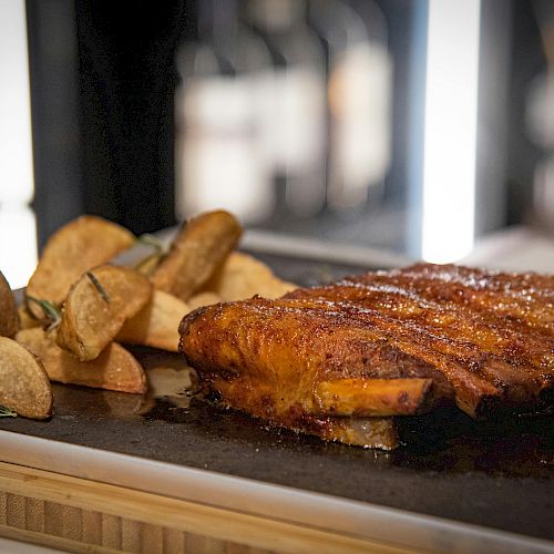 The image shows a roasted meat dish accompanied by wedges of roasted potatoes, garnished and served on a dark platter.