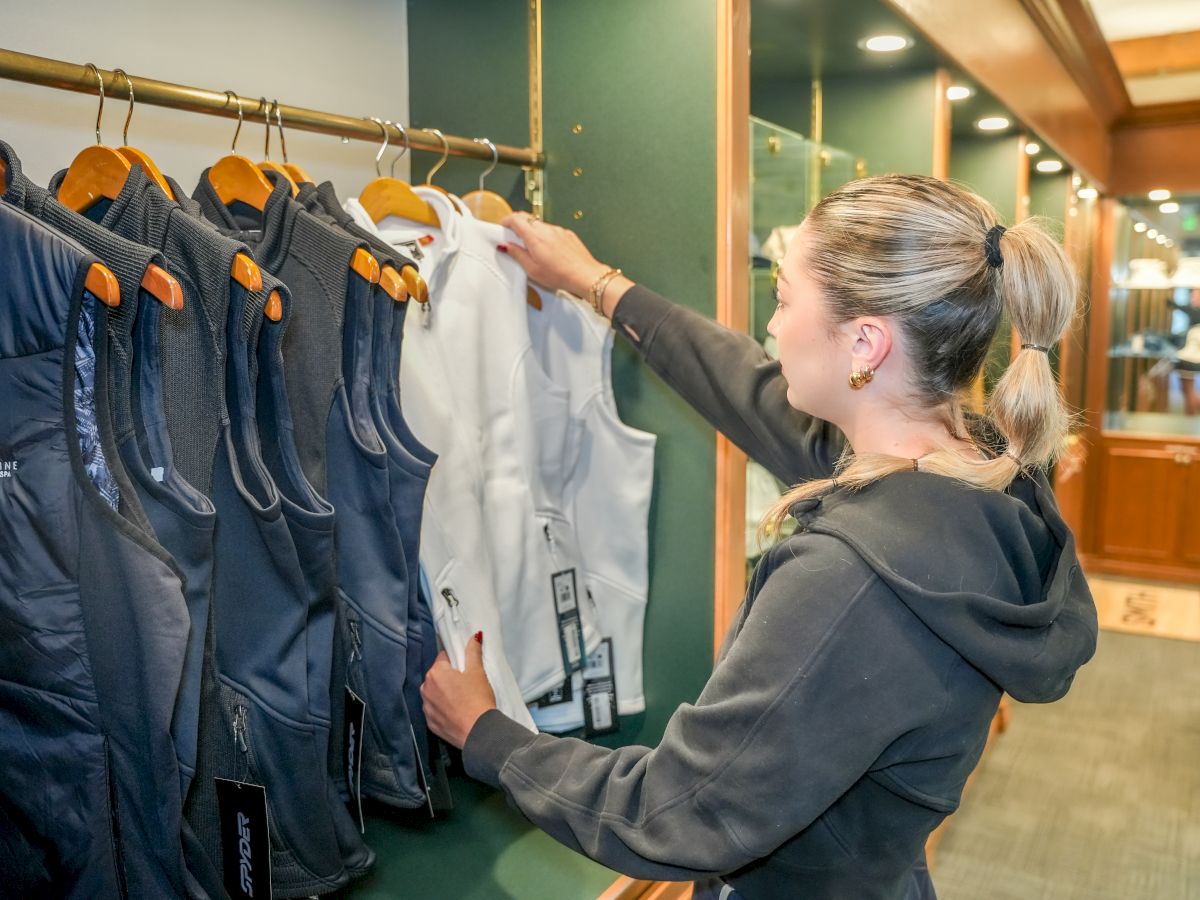 A staff member in a shop adjusts jackets on a clothing rack, with white and dark coats hanging neatly.