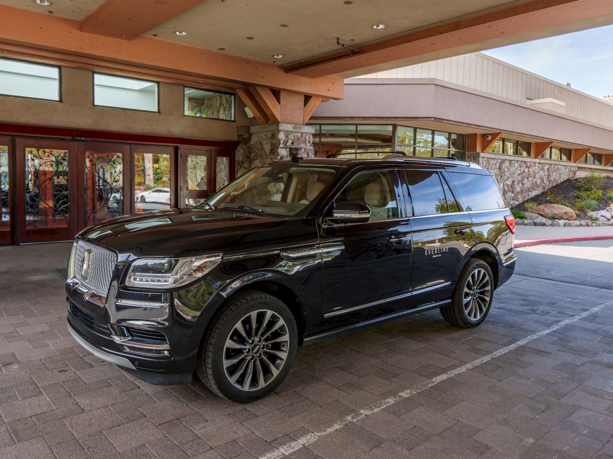 A black SUV/limousine parked outside a modern building with large windows and a stone wall.