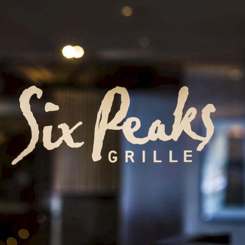 The image shows a sign with the text "Six Peaks Grille" against a blurred background.