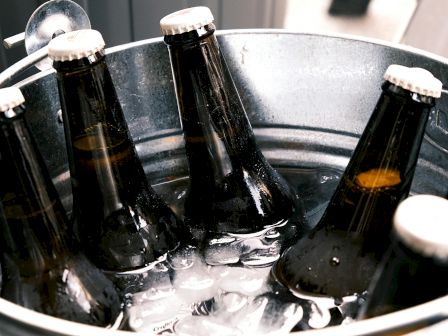 A metal bucket filled with ice holds several dark glass bottles topped with white caps, possibly containing beverages, ready to be served.