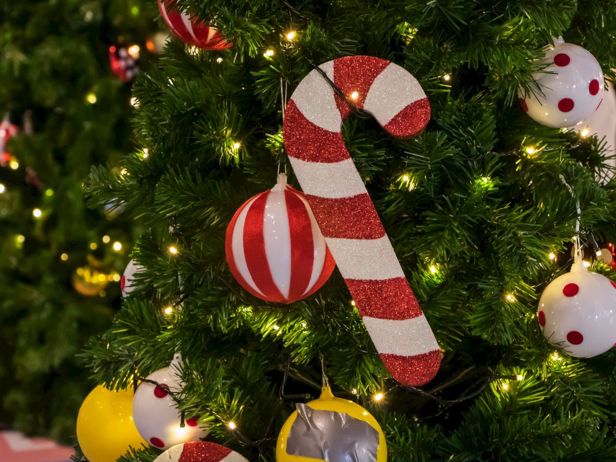 A Christmas tree decorated with a red-and-white candy cane, snowman baubles, and glowing lights, with shiny ornaments all around.