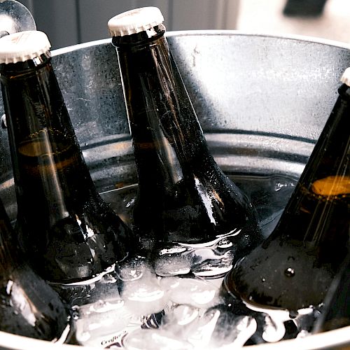 A metal bucket filled with ice contains several capped brown beer bottles.