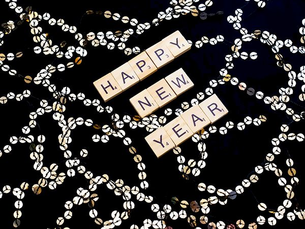 Scrabble tiles spell &ldquo;HAPPY NEW YEAR&rdquo; amid glittery gold-and-silver tinsel decorations.