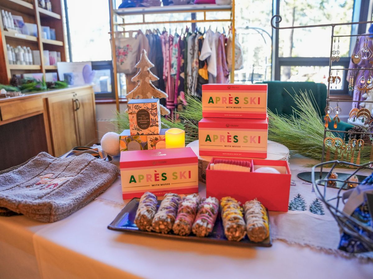 A cozy store display with &ldquo;Apr&egrave;s Ski&rdquo; gift sets, candles, and seasonal decor on a table near the window.