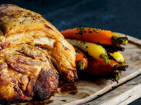 Roasted chicken on a wooden board with roasted carrots and herbs, ready to serve.