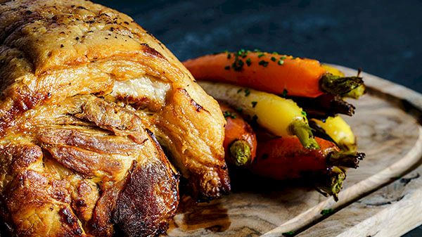 Roasted chicken on a wooden board with roasted carrots and herbs, ready to serve.