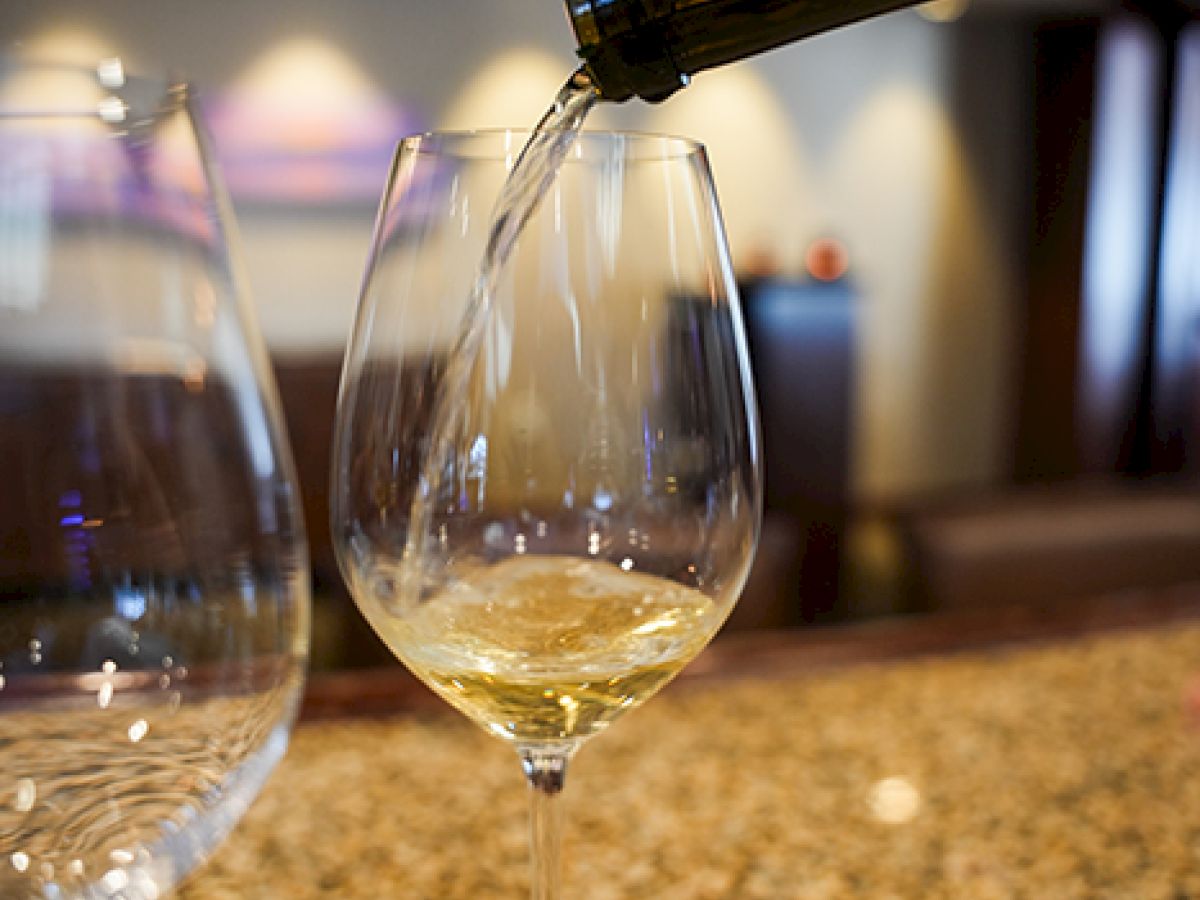 Wine is poured into a stemmed glass at a bar, with two empty glasses nearby.