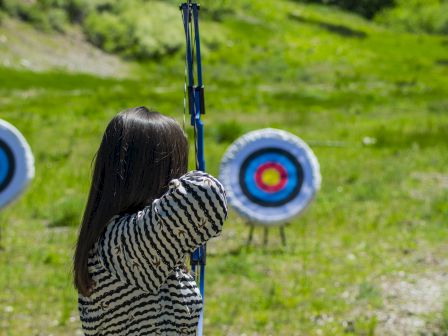 A person practicing archery outdoors, aiming at circular targets on a grassy field.