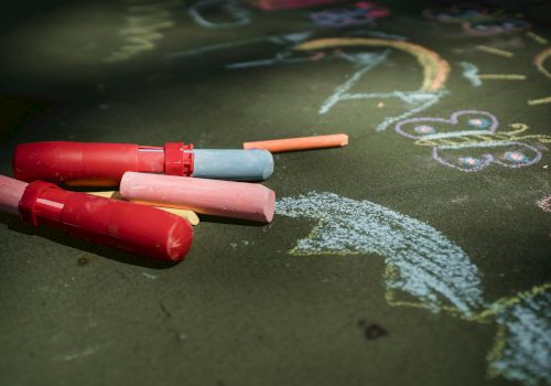 Colorful chalks and various drawings, including a butterfly and a rainbow, are on a green surface.