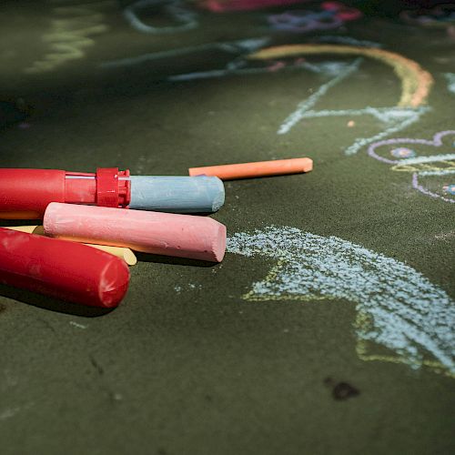 Colorful chalks and various drawings, including a butterfly and a rainbow, are on a green surface.