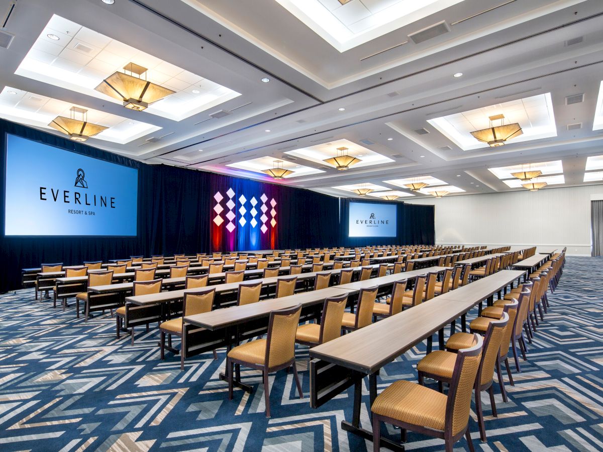 This image shows a large conference room with rows of tables and chairs facing two projection screens, featuring "Everline" branding.