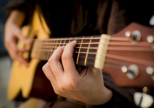 A person plays an acoustic guitar, focusing on the frets and strings, creating music with their fingers on the instrument.
