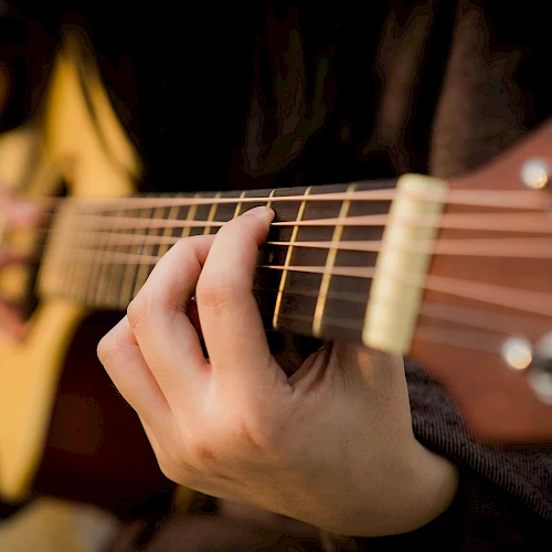 A person plays an acoustic guitar, focusing on the frets and strings, creating music with their fingers on the instrument.