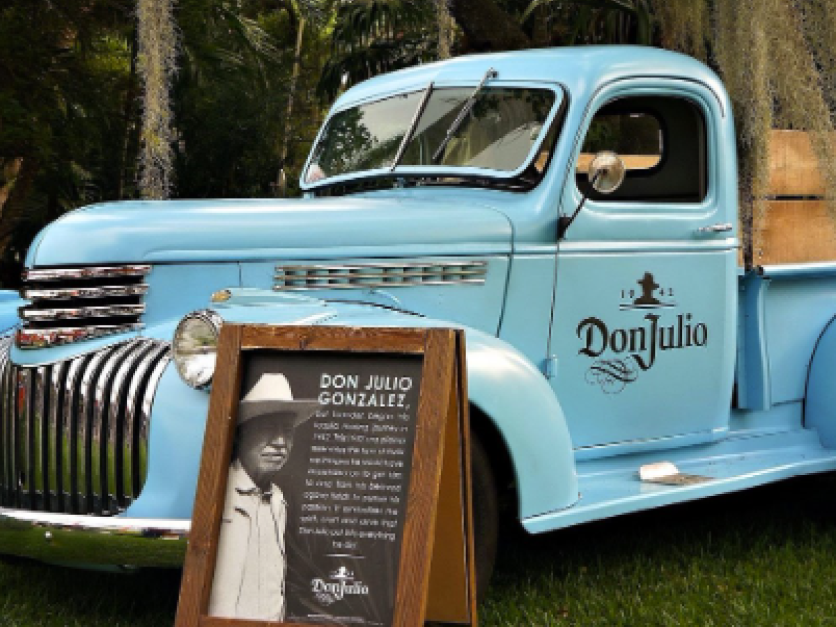A vintage blue truck with "Don Julio" branding, parked on grass, next to a sign with information about Don Julio Gonz&aacute;lez.