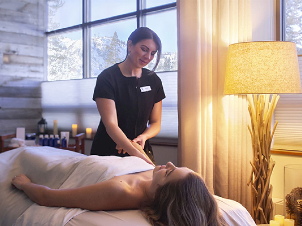 A person receives a massage in a cozy spa room with soft lighting, candles, and a nature-themed decor.