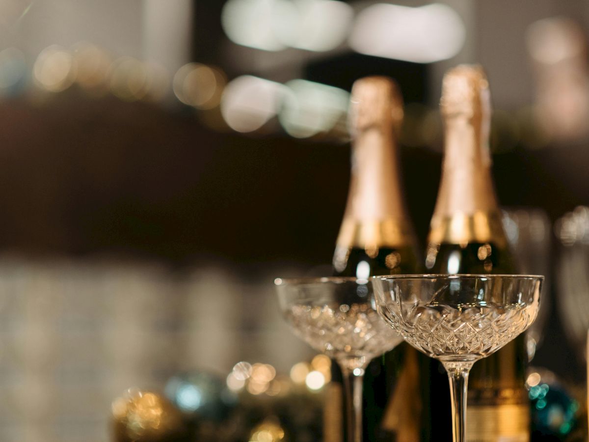 Two champagne bottles and two crystal glasses are on a table, blurred background with festive decorations.