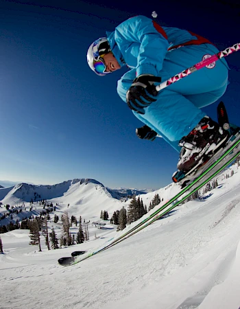 A skier in blue attire is captured mid-jump on a snowy slope under a clear sky and bright sun.