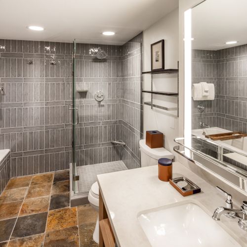 The image shows a modern bathroom with a bathtub, glass shower, and a large mirror above a sink.
