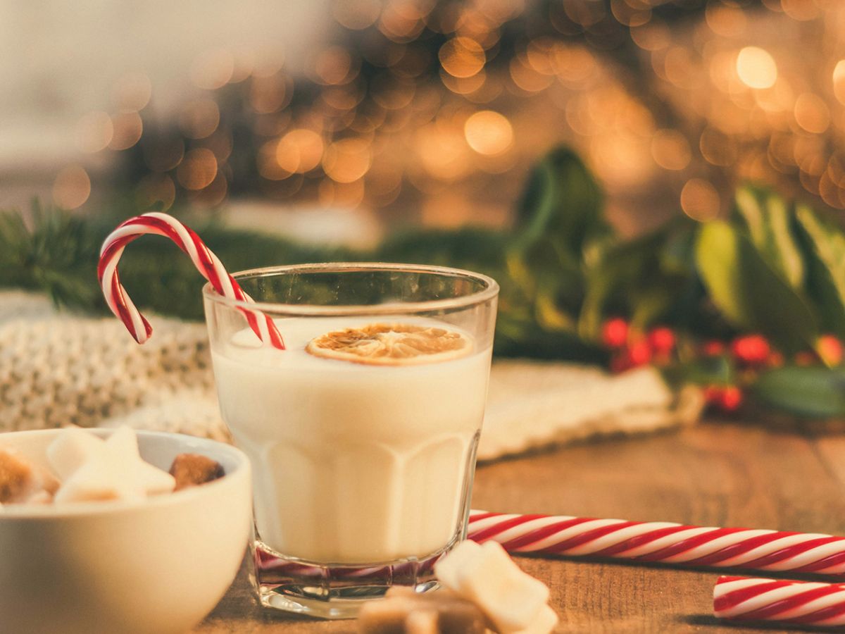 A festive setting with a glass of milk or eggnog, candy canes, a bowl of marshmallows, and holiday decorations on a wooden table.