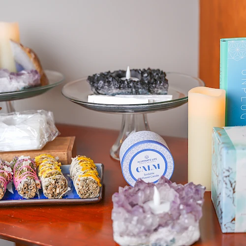 A cozy display of spa treats: two decorative cakes on stands, colorful rolled sweets, wrapped bars, candles, crystals, and a turquoise spa box, all arranged invitingly.